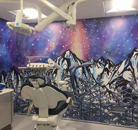 A dental chair in front of a wall painted with a bright mural of Alaskan landscape