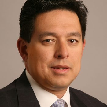 A man with black hair wearing a white shirt and black suit smiles for the camera. 