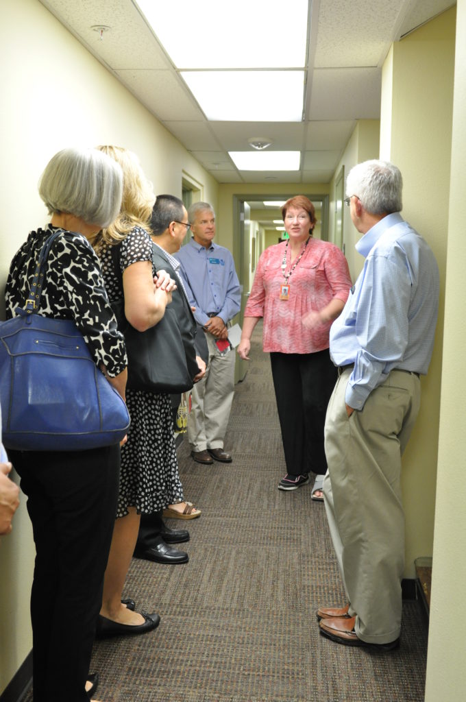 Five adults stand in a hallway while someone gives them a tour. 