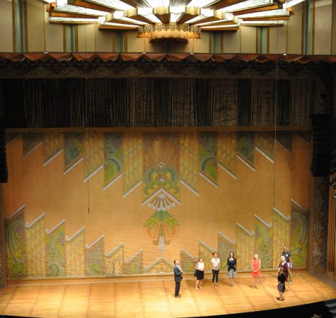 Several adults on the stage of a historic theater.