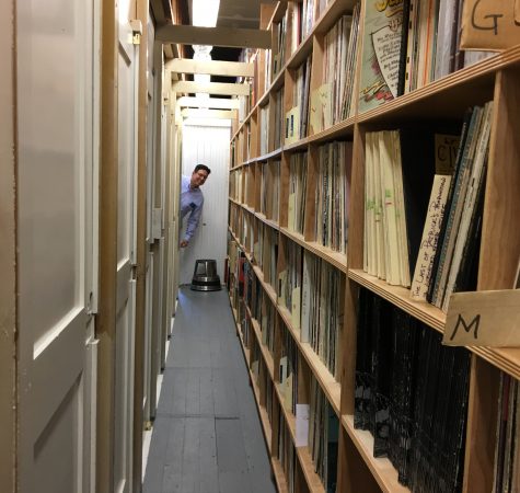 A man peeks out behind a row of shelves filled with record albums.