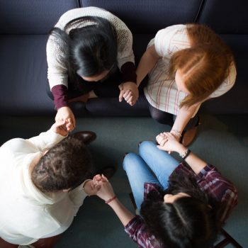 An overhead shot of four students holding hands and praying. 