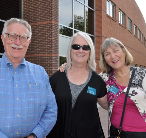 A man with gray hair wearing glasses and a blue shirt, a woman with straight white air wearing sunglasses and a black shirt, and a woman with short gray hair wearing a pink shirt smile for the camera.