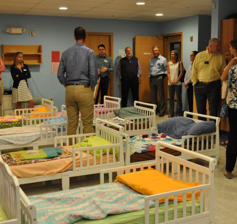 A group of people receive a tour of the nursery facility, standing inside a room with empty beds.