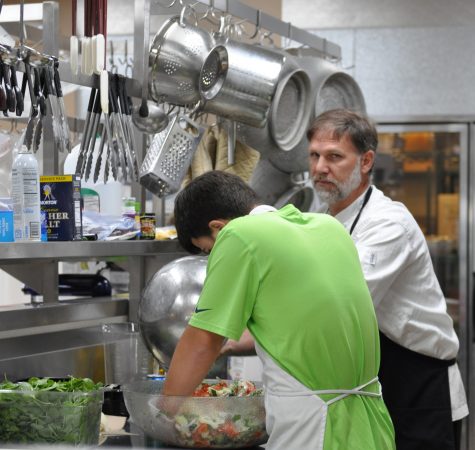 Two people prepare a meal inside an industrial kitchen.