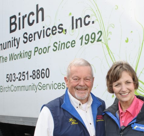 A man wearing a white shirt and gray vest and a woman wearing a pink shirt and gray jacket smile for the camera in front of a sign that says "Community Birch Services, Inc."
