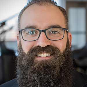 A man with a beard and glasses smiles for the camera. 