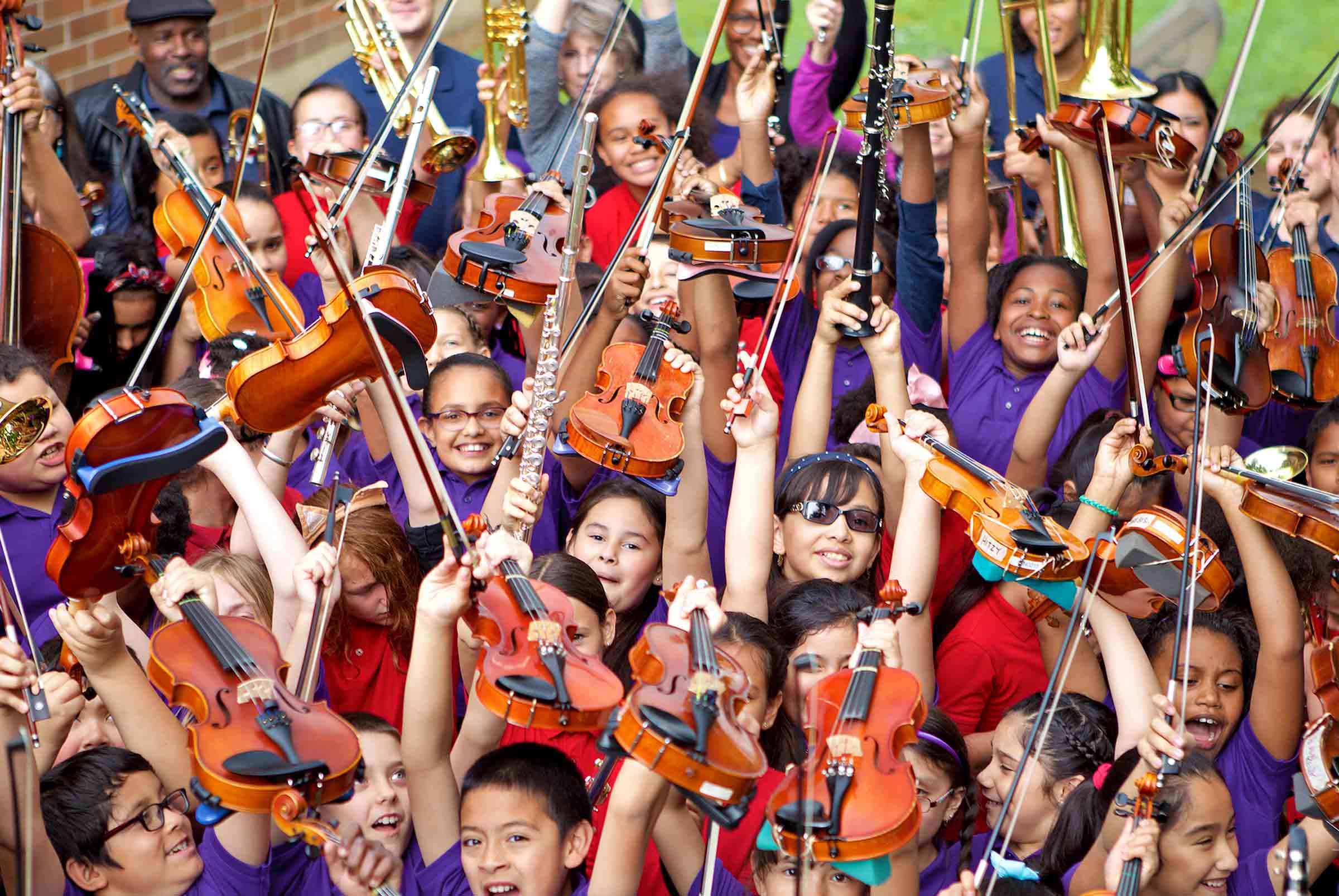A group of children wearing purple shirts hold up instruments and smile for the camera. 