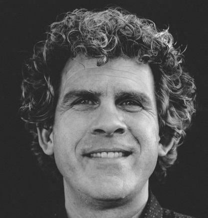 A black and white photo of a man with curly hair smiling at the camera. 