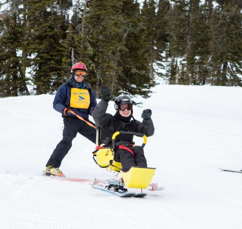 An instructor guides a child with disabilities on a specially designed ski sled