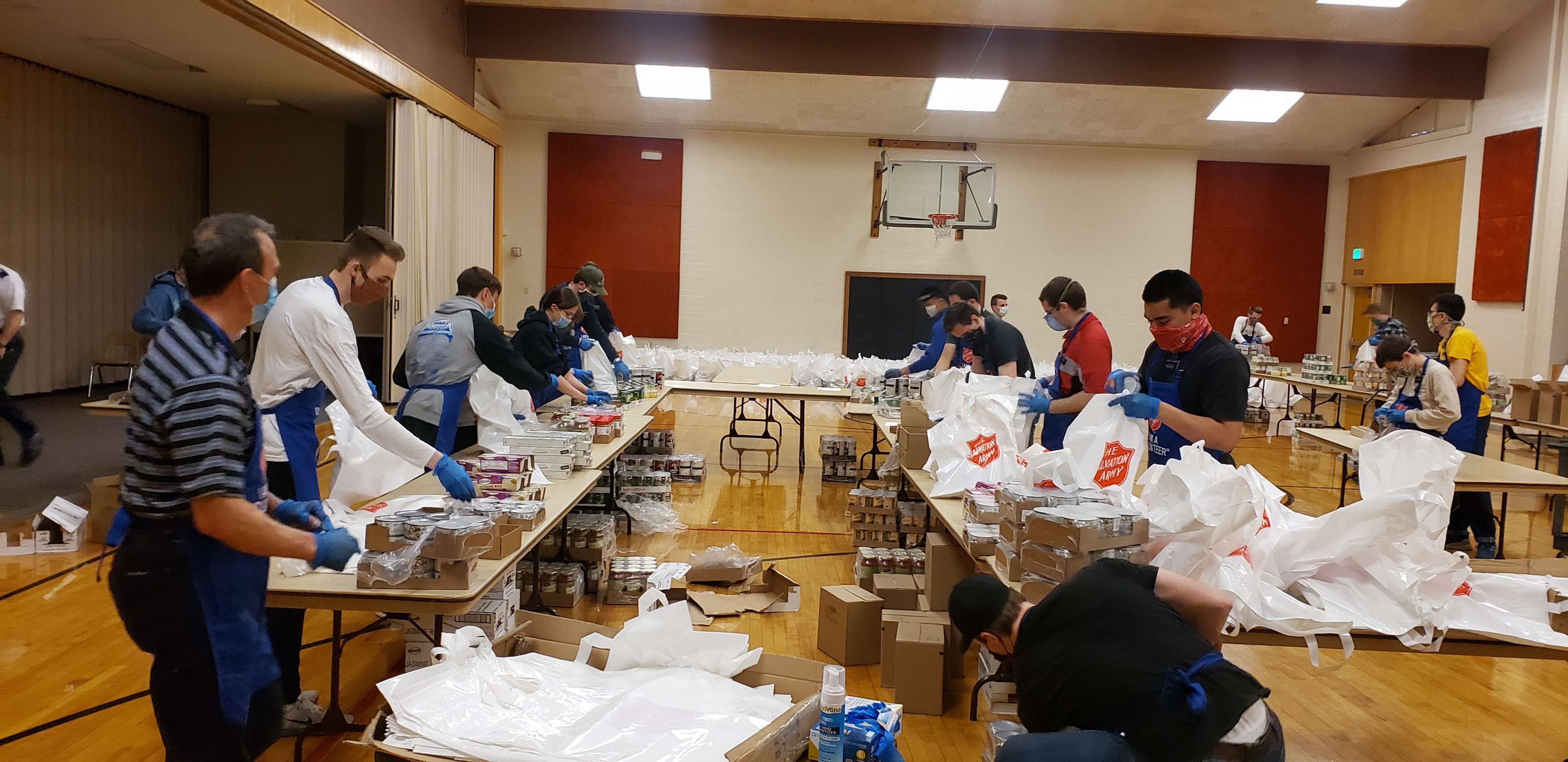 A group of volunteers gather food packages in a gymnasium