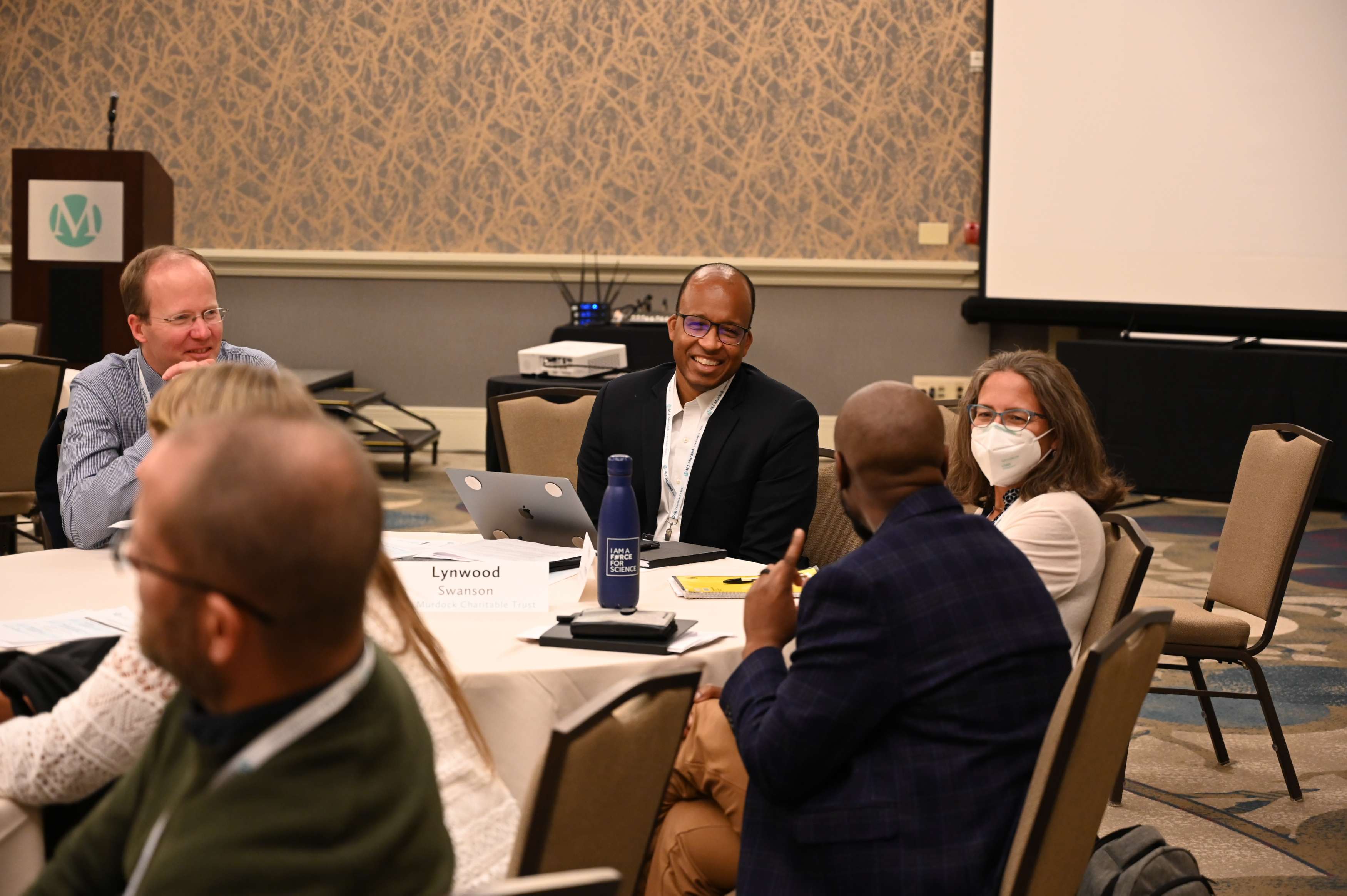 A group of participants laugh and have conversation around a table at the Scientific Research and Christian Faith convening. 