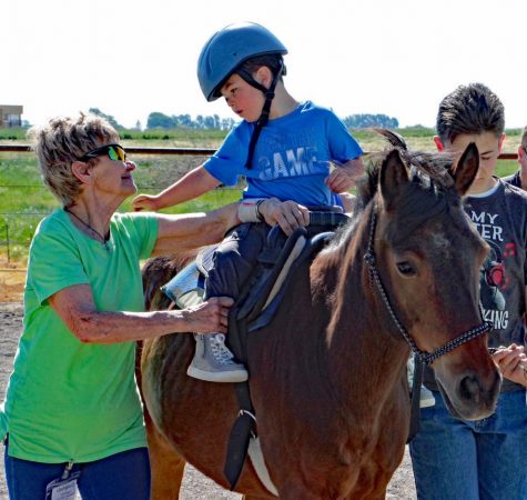 A child wearing a blue shirt and helmet rides a horse while a woman wearing a green shirt assists. 