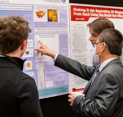 A man wearing a gray suit and a mask points to something on one of the 2022 MCSR Conference poster presentations.
