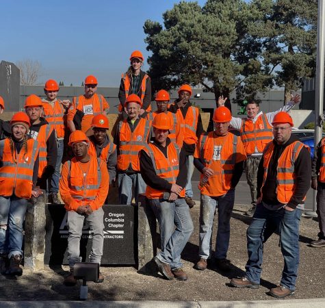 A group of program participants from Constructing Hope, all wearing orange reflective gear and hard hats, smile for the camera outside.