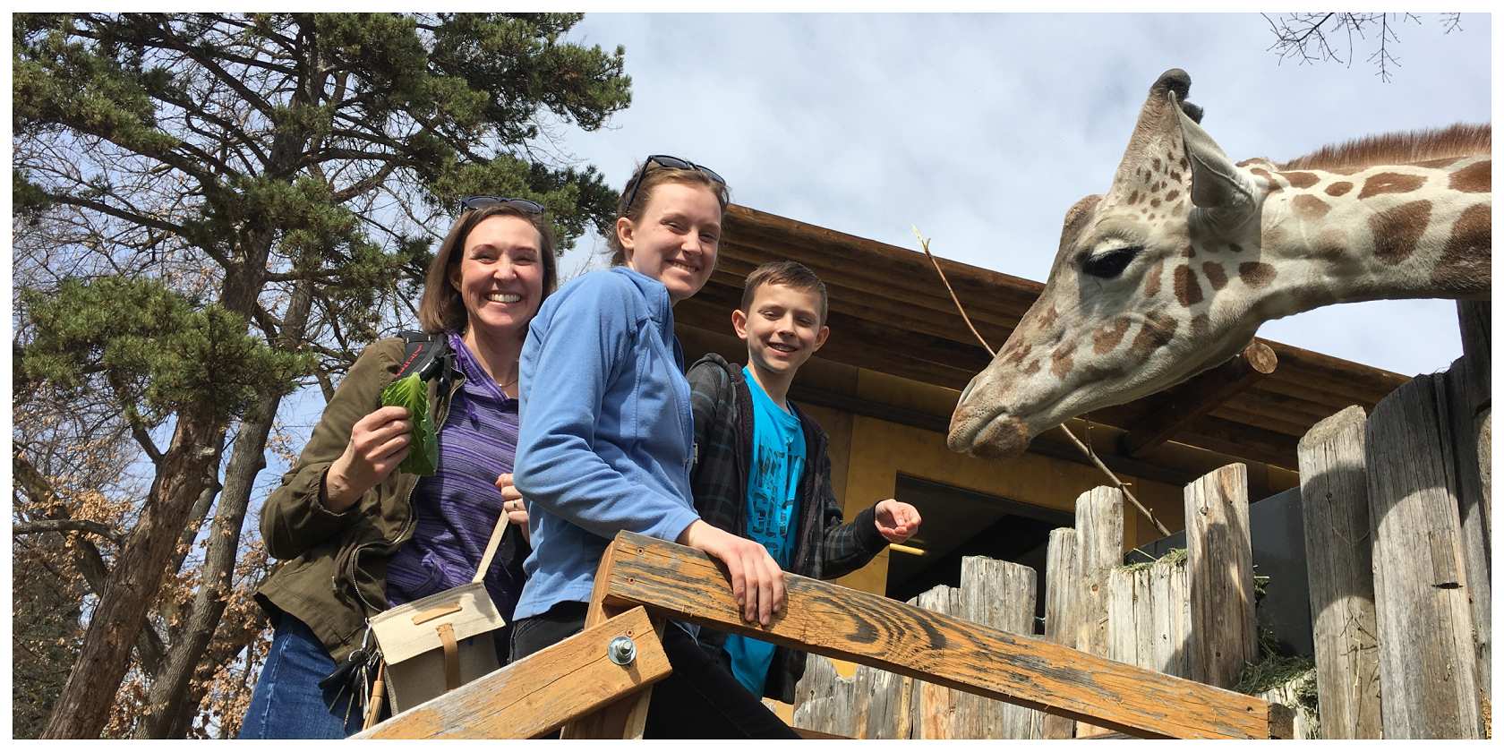 A photo from Zoo Boise, a Fall 2022 Murdock Trust grantee, of three people smiling next to a giraffe