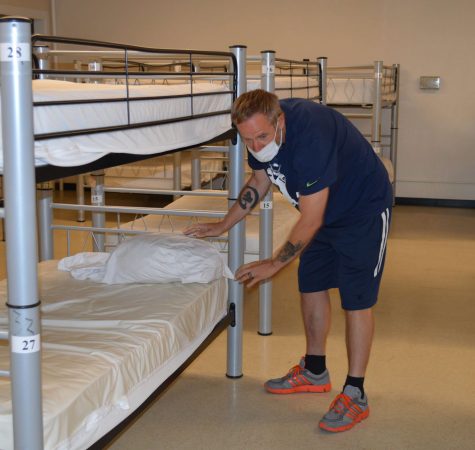 A man wearing a mask puts new sheets on a bunk bed at Montana Rescue Mission.
