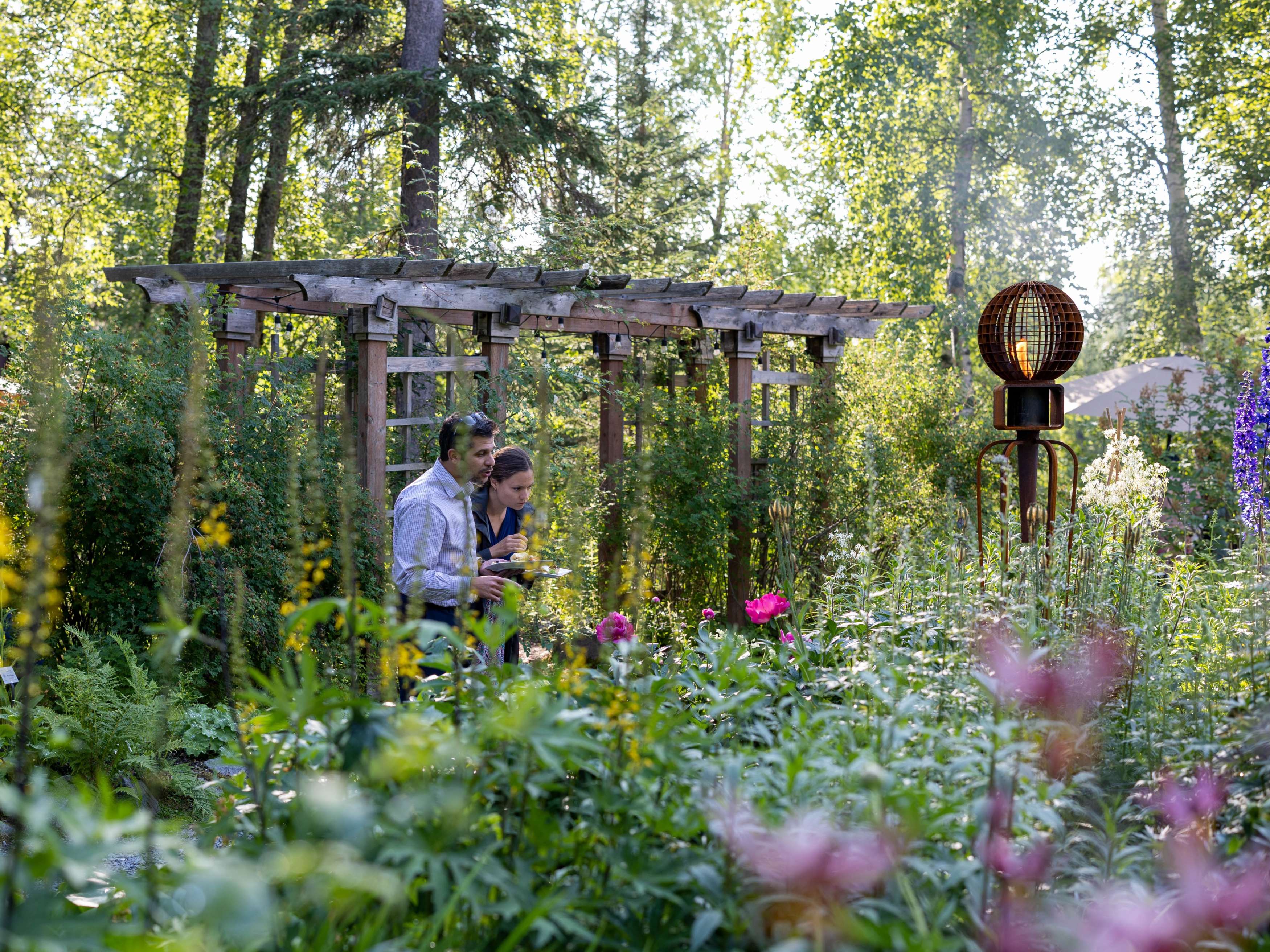 Two adults walk through a botanical garden with a wooden structure behind them.