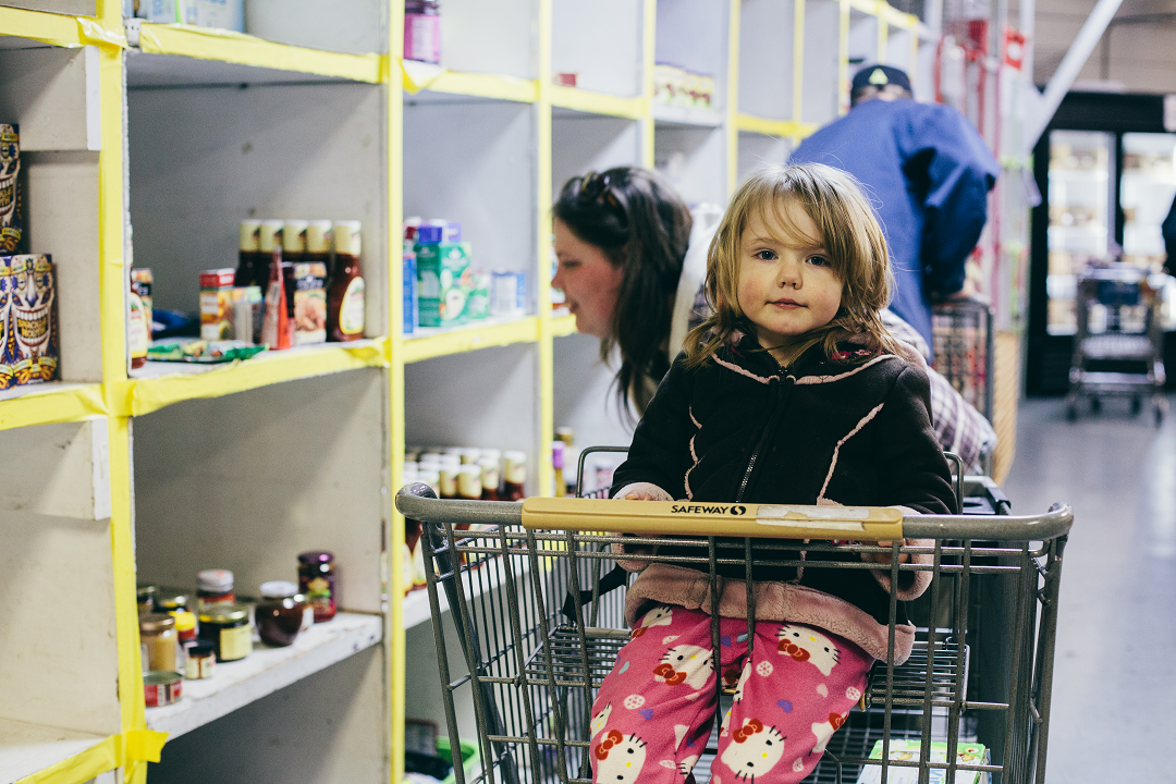 A child sits in a shopping cart inside a food pantry