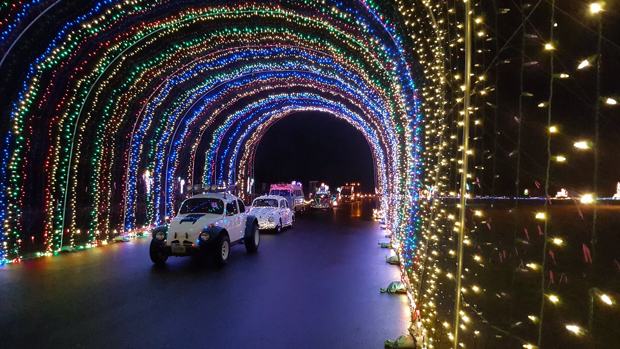 Volkswagons drive through a lights show at night.