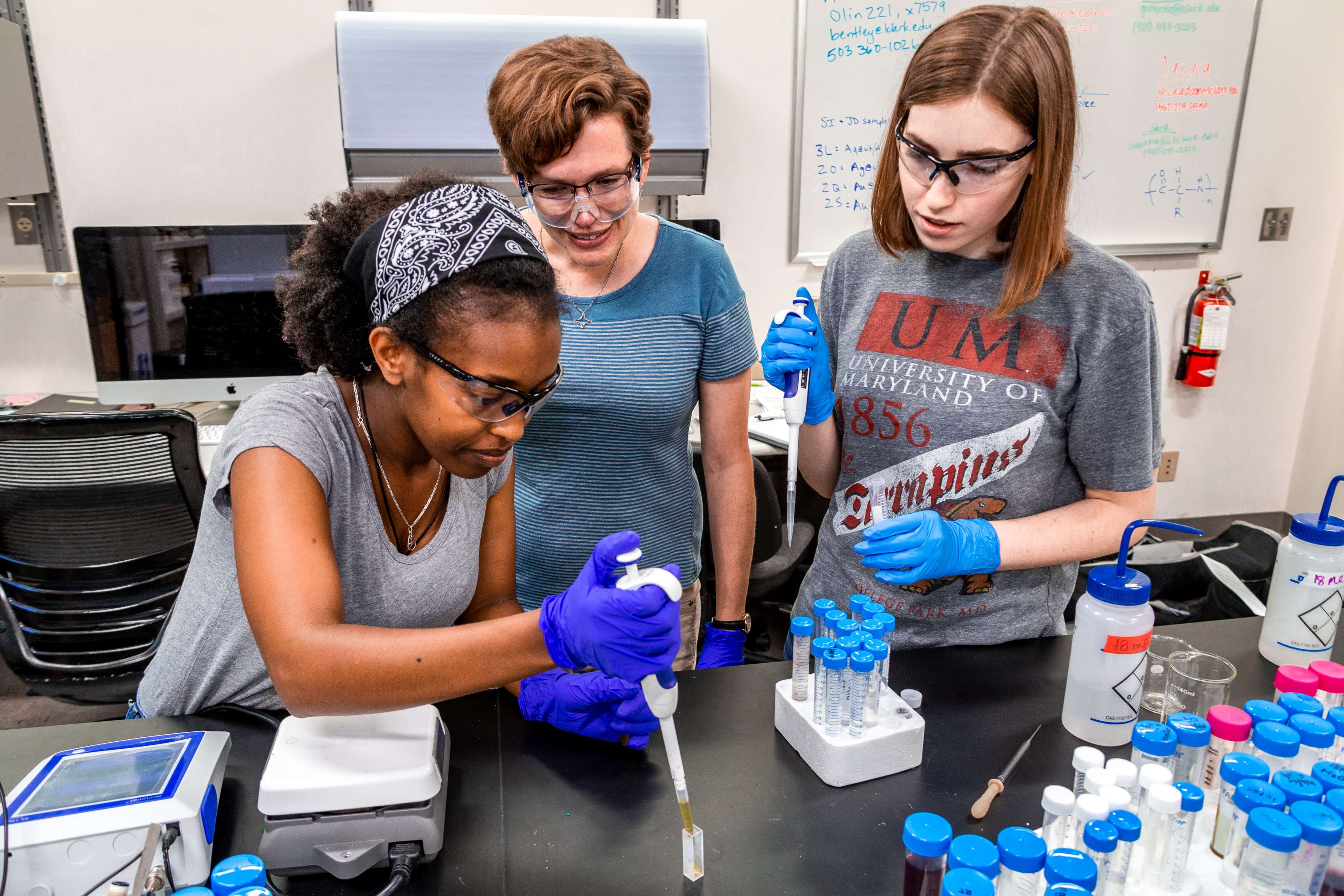 Three female college students doing research in a classroom wearing gloves and protective eyewear