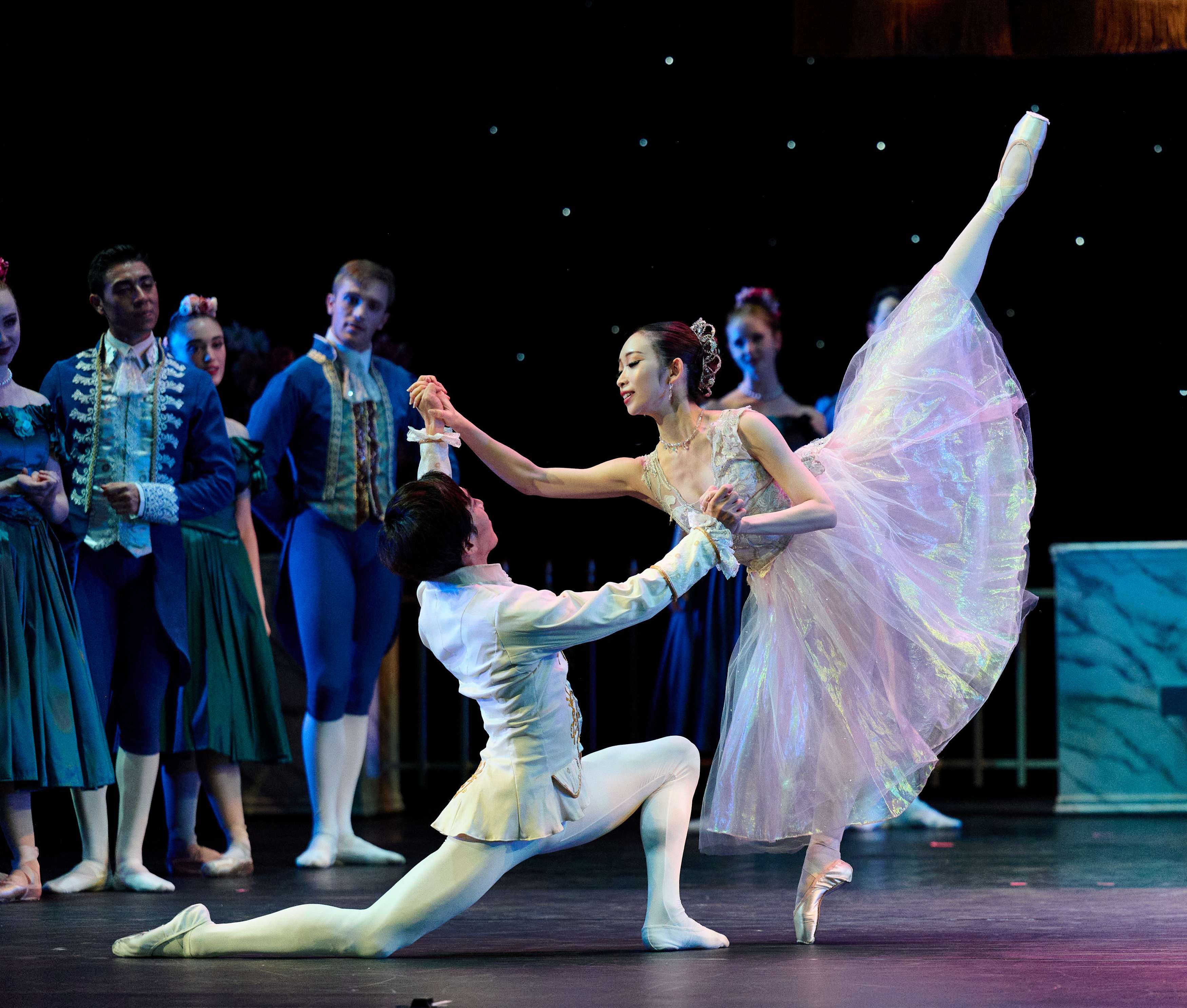 Ballet performance of Cinderella, with the male performer in white on the ground and the female performer holding his hands with one foot in the air