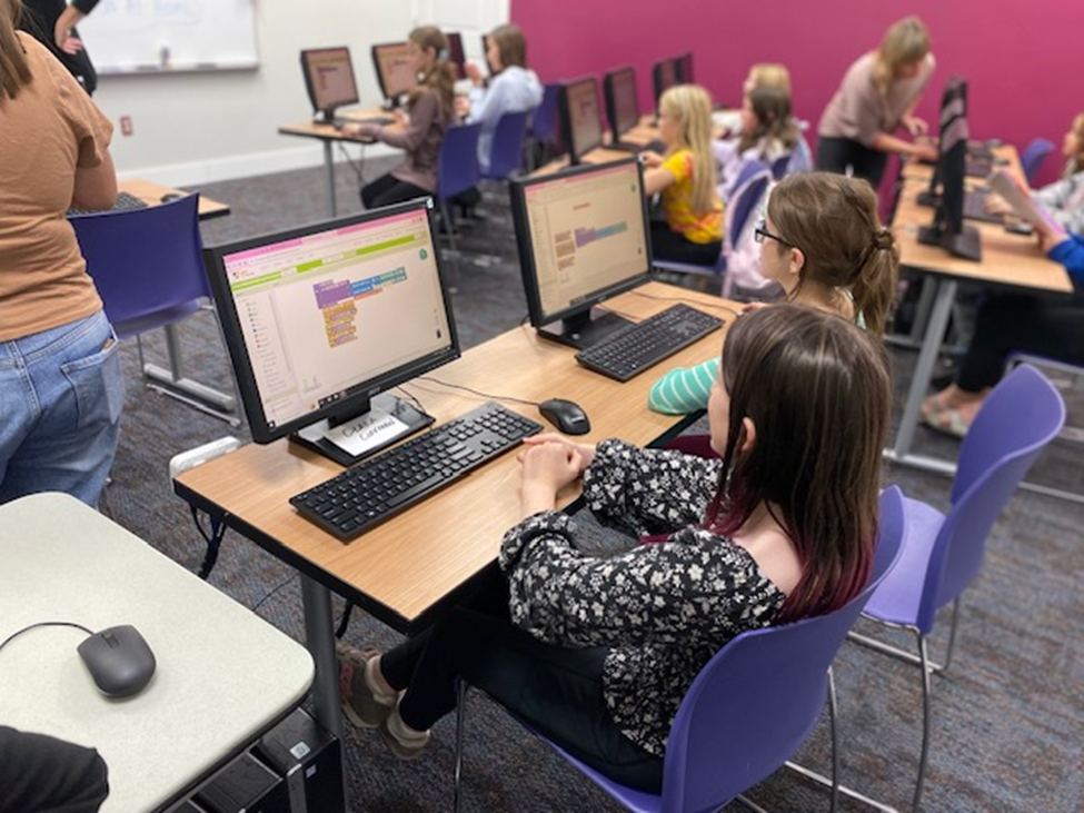 A classroom of young girls learning to code on computers