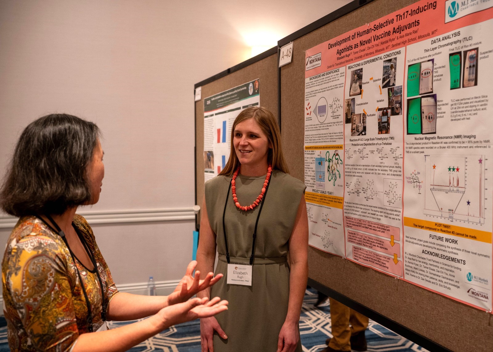 Two individuals engaging in a discussion at a scientific conference poster session. One person is standing by a poster that includes various graphs and diagrams related to vaccine development. 