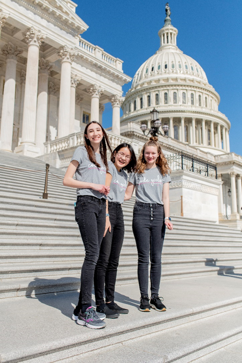 Three smiling girls in Code Girls United shirts on the steps of Congress