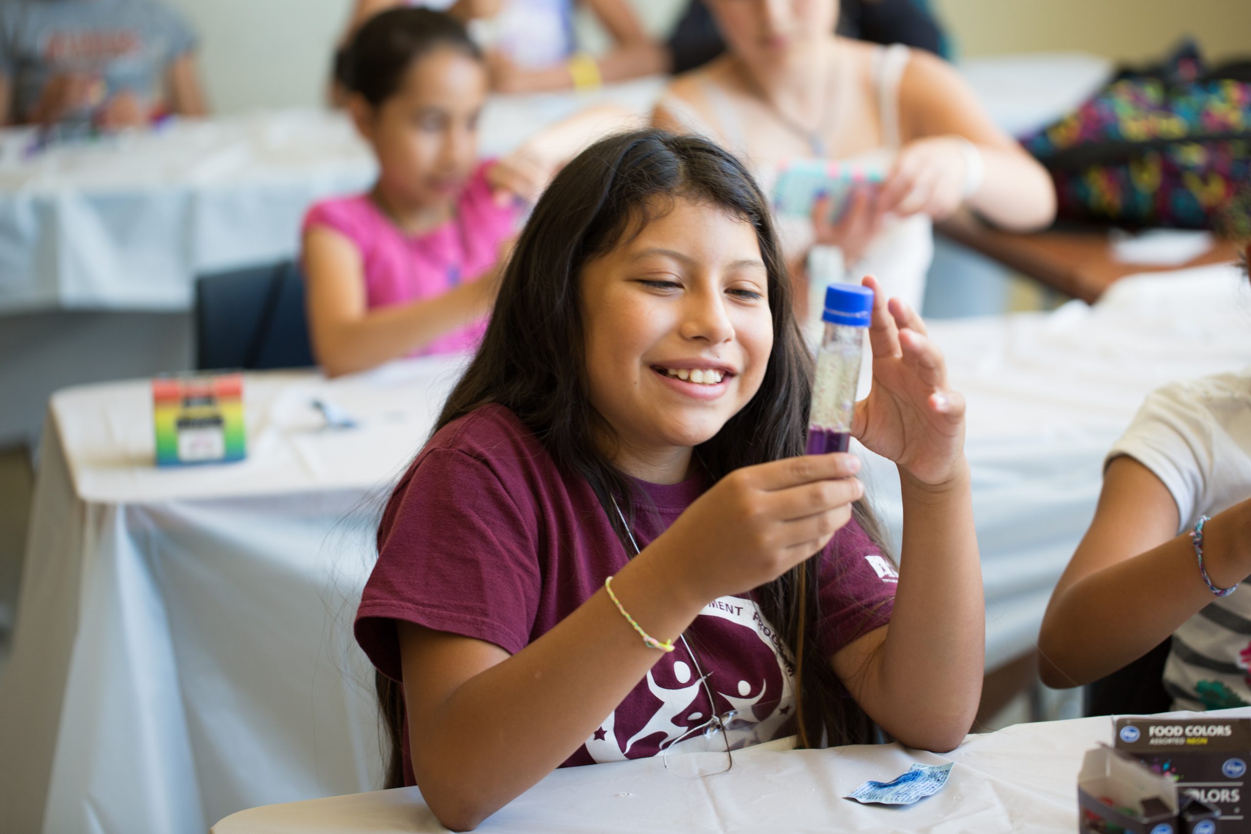 Kid with test tube partially filled with liquid, smiling and sitting at a table