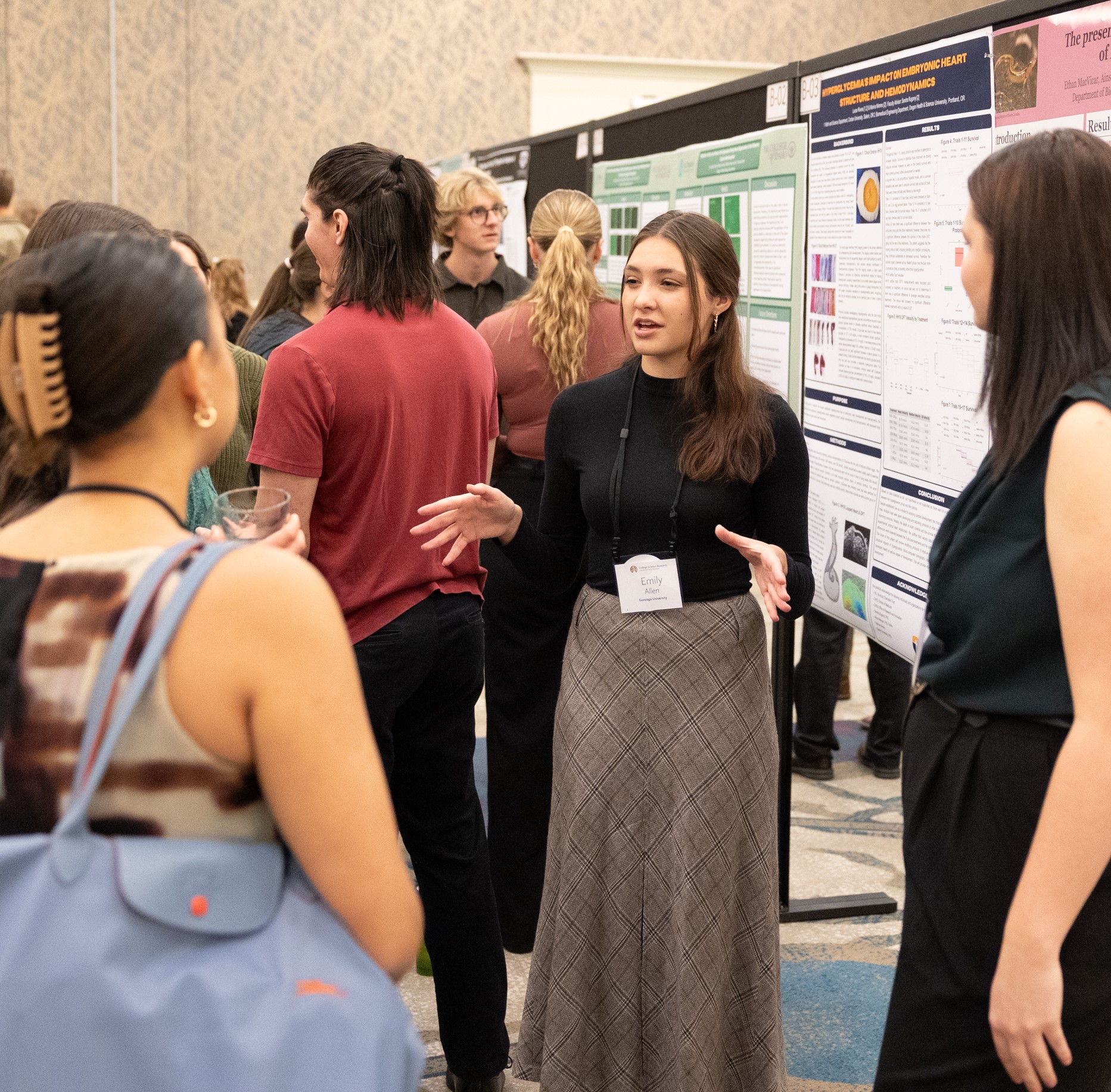 Student next to poster with scientific research, presenting to a small group of people listening intently