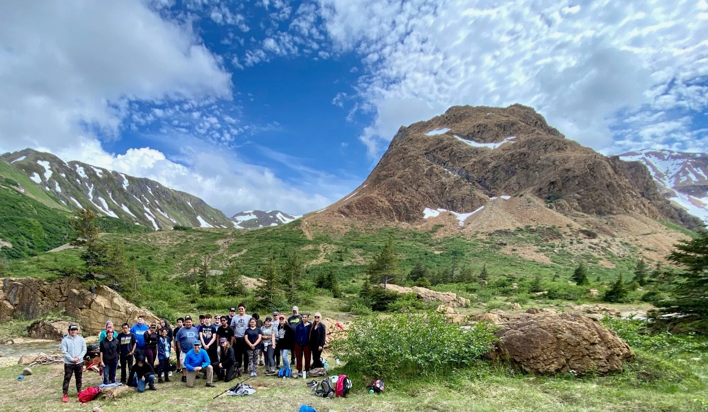 Group of people standing in outdoor environment with sunny sky and mountains behind them