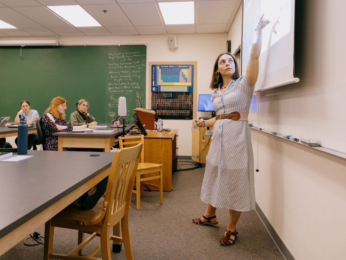 Jessica Sutter, a professor at Whitman College, pointing to a projector screen as she teaches a classroom full of students.