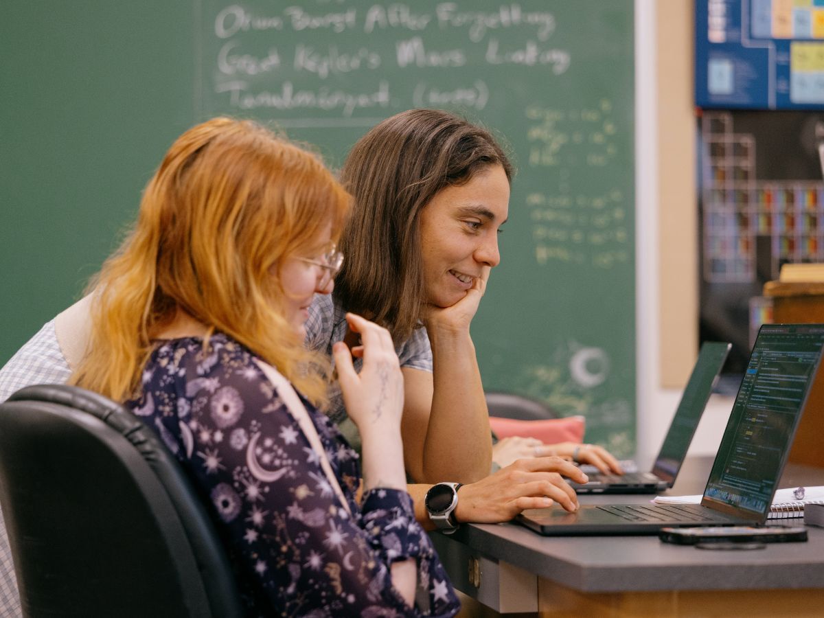 Jessica Sutter, a professor at Whitman College, sits beside a student as they work together on laptops at a table.
