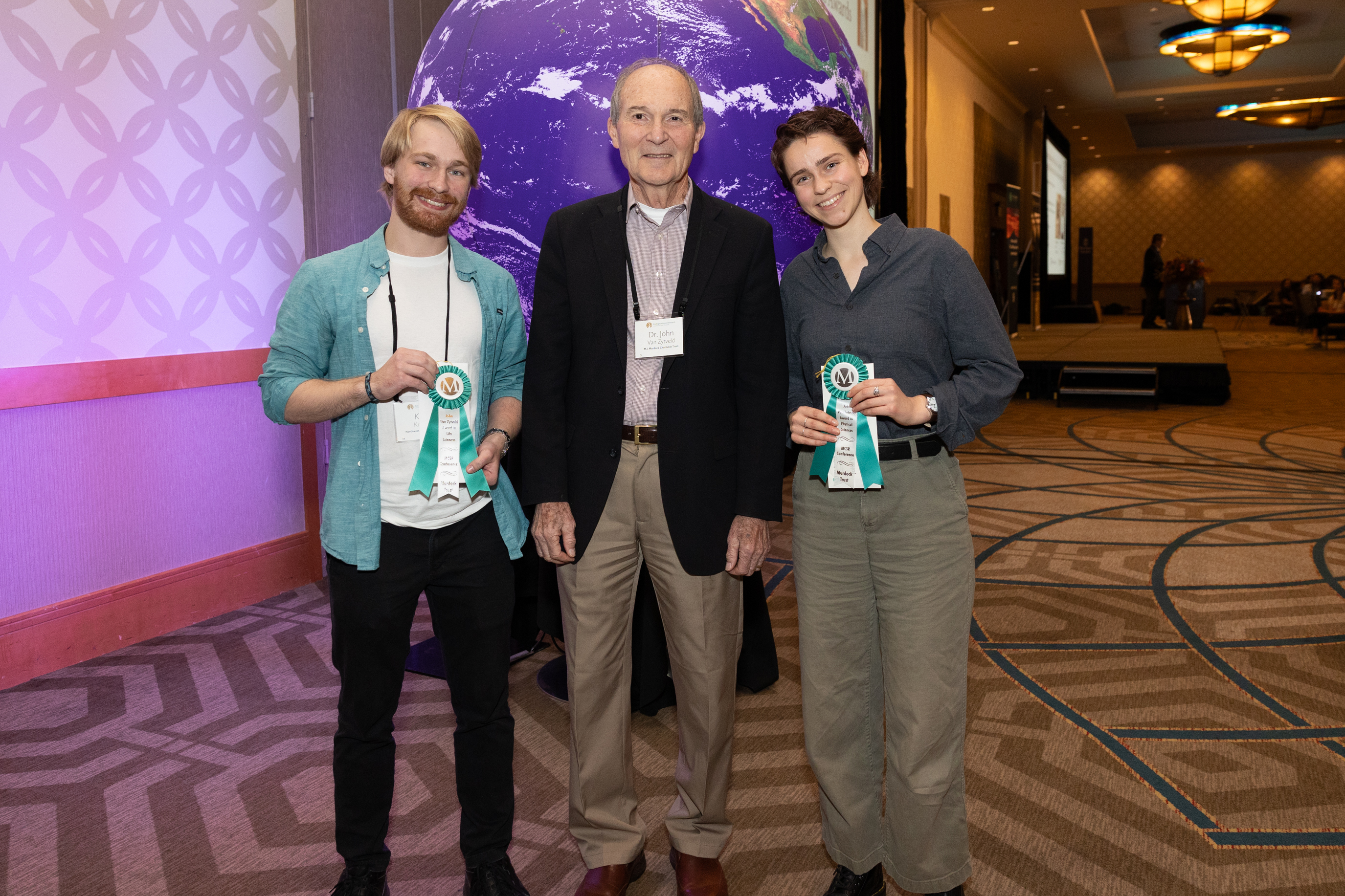 Three people standing in a conference room, with the two people on the outside holding a ribbon and smiling