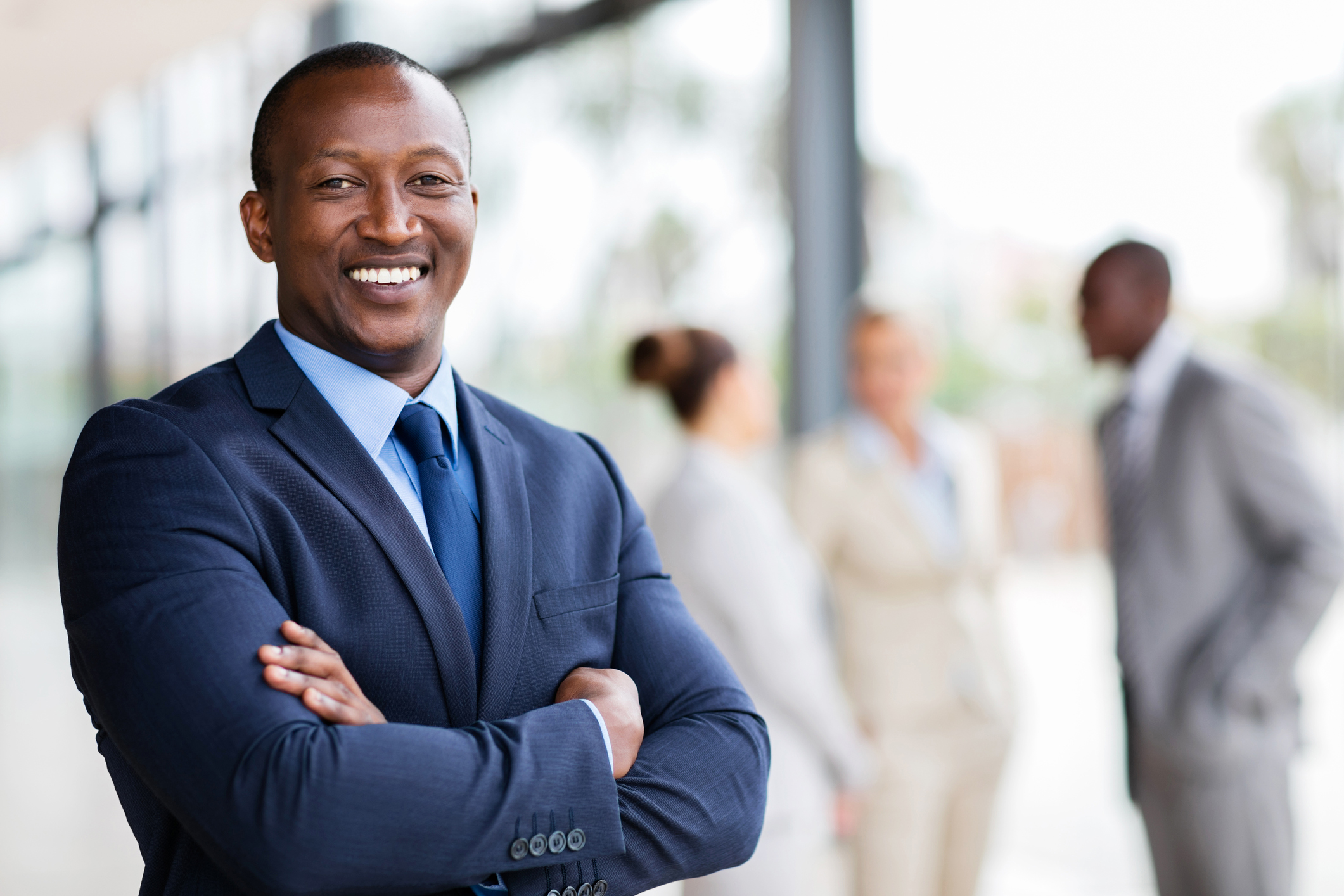 A man with dark skin wearing a blue suit smiles for the camera.