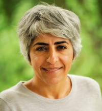 A woman with short gray hair wearing a light gray shirt smiles for the camera.