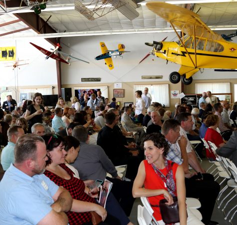 A large group of people gather inside a Museum of Flight facility