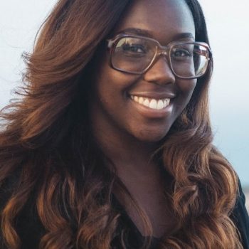 A woman with long dark hair wearing glasses and a black shirt smiles for the camera.