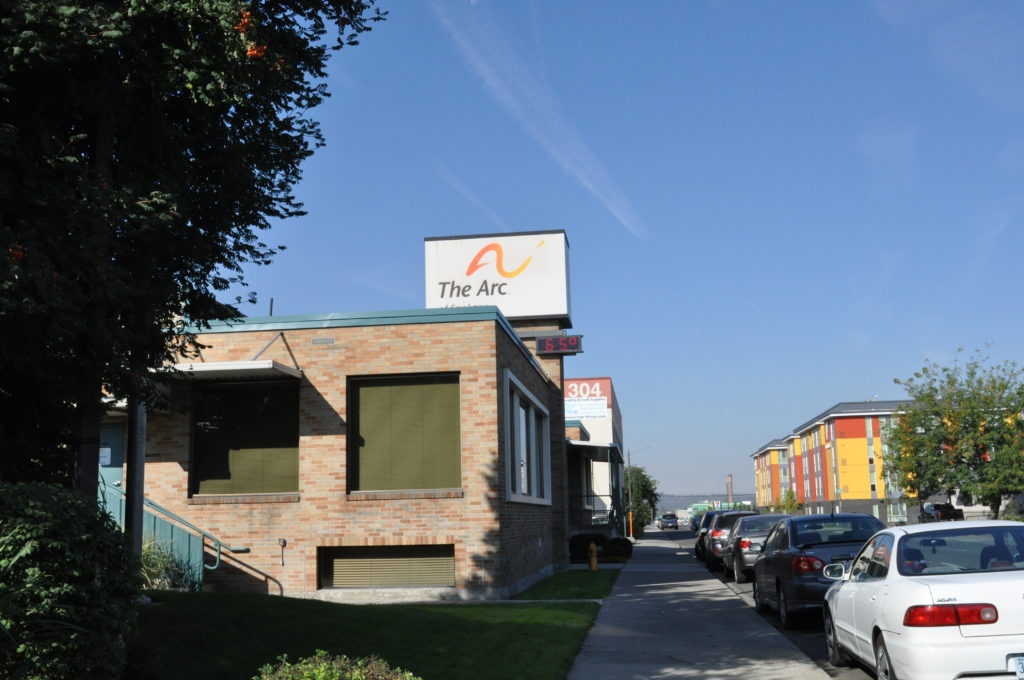 A square building labeled "The Arc" on a street with cars parked along the curb.