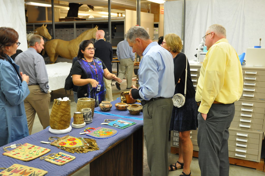 A group of adults looking at artifacts on a long blue table.