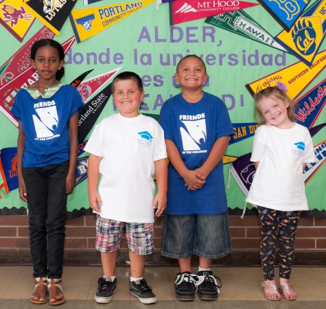 Four young children smile in front of a colorful wall of posters.