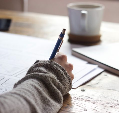 A close-up photo of someone writing on a piece of paper, with a coffee mug in the background.