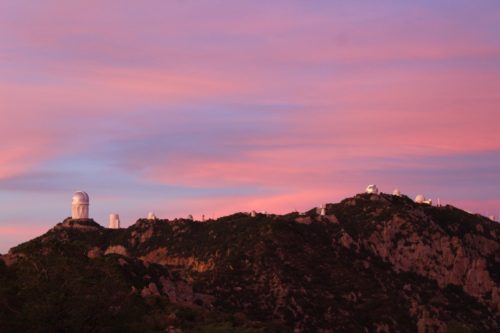 A sunset behind a large hill with an observatory on it.