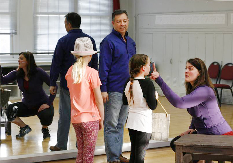 Two adults and two young girls in front of a mirror in an acting studio.