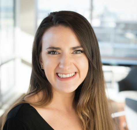 A woman with straight dark hair smiles at the camera in an office.