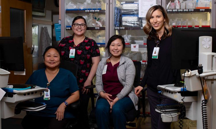 Four female nurses smile at the camera from inside a lab.