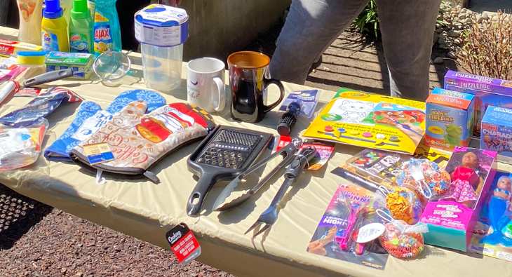 Oven mitts, kitchen utensils, dolls, cleaning supplies, and other assorted items on a table.