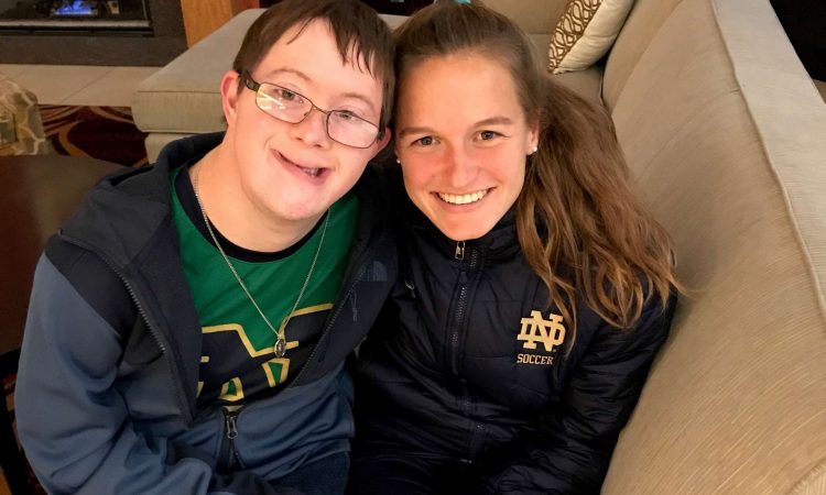 A young woman and boy smile for the camera while sitting on a couch.