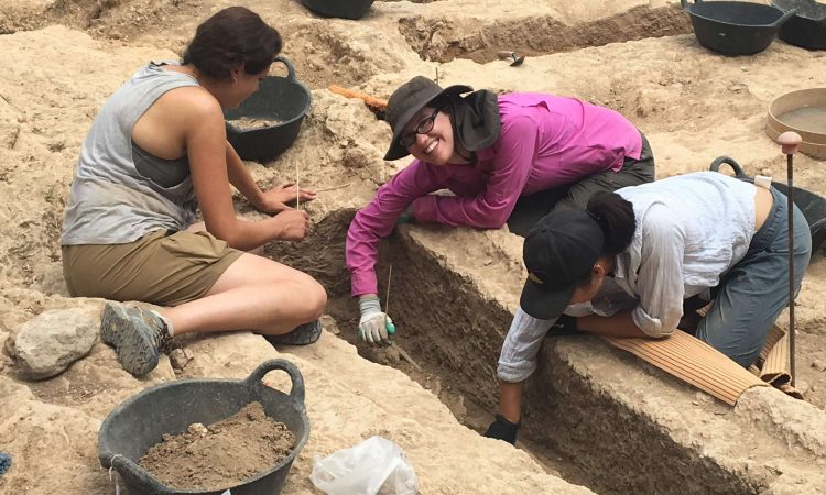 Three adults gather soil at an excavation site.